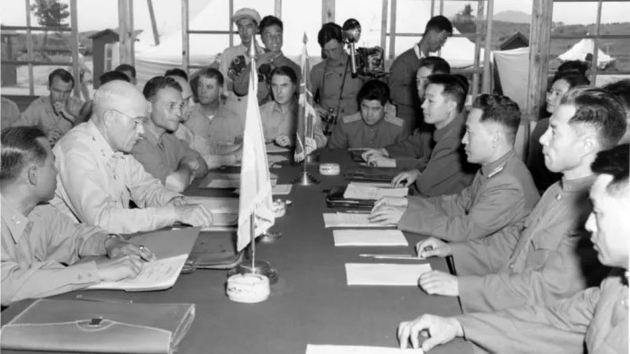 This image depicts the Korean War armistice negotiations, which took place between United Nations Command (UNC) representatives and North Korean/Chinese officials. The talks, held at Panmunjom, began in 1951 and culminated in the signing of the Korean Armistice Agreement on July 27, 1953. This agreement ended active hostilities and established the Demilitarized Zone (DMZ), although a formal peace treaty was never signed, leaving North and South Korea technically still at war.