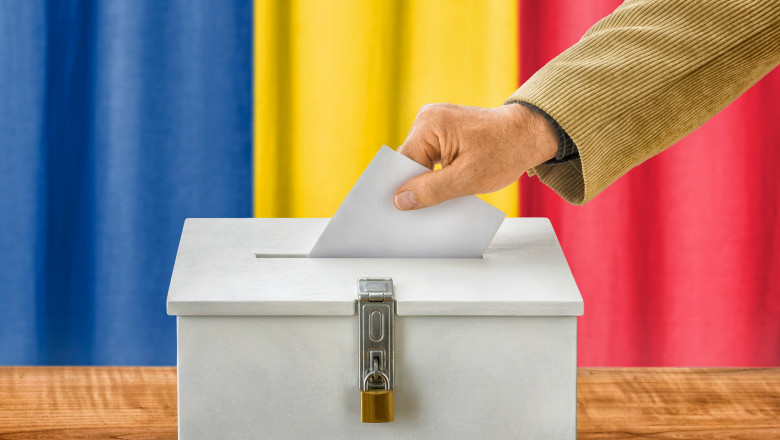 Aceasta este o imagine care surprinde un moment simbolic al procesului electoral, în care o persoană introduce un buletin de vot într-o urnă albă, simbolizând exprimarea dreptului democratic de a vota. În fundal, se observă culorile drapelului României – roșu, galben și albastru – care subliniază importanța alegerilor prezidențiale din România. Urna are un design simplu, cu un lacăt de siguranță, ce reflectă transparența și securitatea procesului electoral.

Această scenă evocă un moment-cheie în democrație, subliniind participarea cetățenilor la viitorul politic al țării lor.