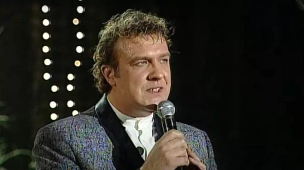 Gabriel Cotabiță interpretând pe scenă, cu microfon în mână, în timpul unui concert memorabil, simbolizând cariera sa emblematică în muzica românească